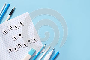 Text Back To School written by printed letters on white sheets of paper on notebook with blue school stationery on blue background