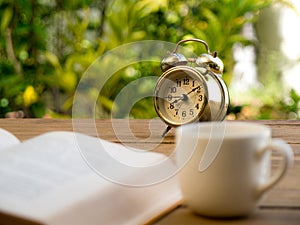 Text book with vintage alarm clock and White coffee cup on the wood table.