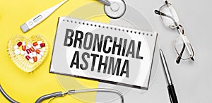 Text bronchial asthma on notebook with stethoscope,glasses, pen,thermometer, red pills and pen on yellow background. Medical