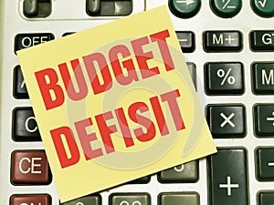Text BUDGET deficit written on yellow paper note on calculator. photo