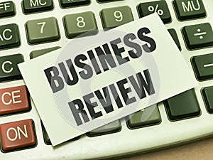 Text BUSINESS REVIEW written on white paper note on calculator. photo