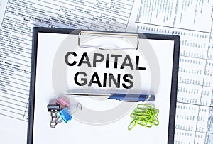 Text Capital Gains on folder with clip. Pen with paper clips on financial table