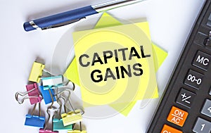 Text Capital Gains on yellow stickers with calculator, blue pen and paper clips