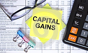 Text Capital Gains on yellow stickers with calculator, eyeglasses and paper clips