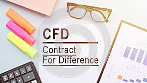 The text CFD - Contract For Difference, on office desk with calculator, markers, glasses and financial charts