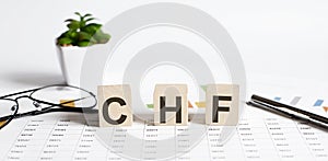 Text of CHF on the wooden cubes on chart with pen and glasses