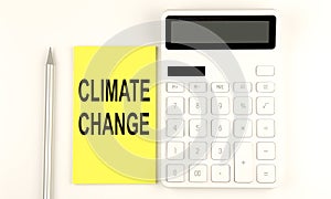 Text CLIMATE CHANGE on yellow sticker, next to pen and calculator