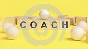 text COACH on wooden cubes. bright yellow surface. wooden sphere balls among the wood cubes, different and position in