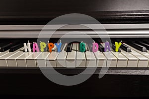 Text from colorful candles `happy birthday` on the piano keyboard.