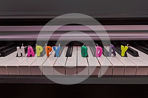 Text from colorful candles `happy birthday` on the piano keyboard.