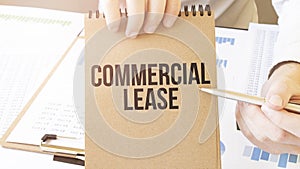 Text commercial lease on brown paper notepad in businessman hands on the table with diagram. Business concept