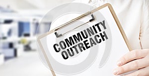 Text COMMUNITY OUTREACH on white paper plate in businessman hands in office. Business concept