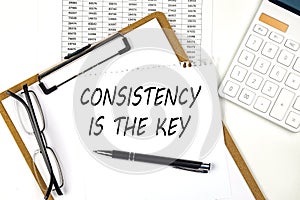 Text CONSISTENCY IS THE KEY on the white paper on clipboard with chart and calculator