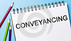 Text Conveyancing on a white notepad with pencils on a blue background. Business concept