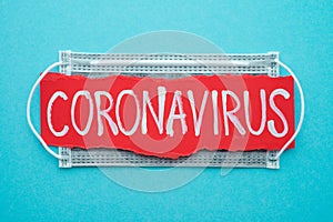 Text CORONAVIRUS with gray protect face mask on blue background with copy space. Global novel coronavirus Covid-19 outbreak