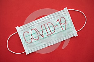 Text COVID-19 on green surgical face mask on red background with copy space. Global novel coronavirus Covid-19 outbreak pandemic