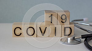 The text COVID-19 on wooden toy cubes, next to a stethoscope