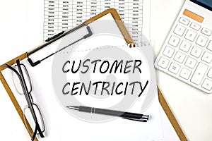 Text CUSTOMER CENTRICITY on the white paper on clipboard with chart and calculator