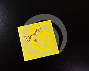 Text Danke on sticky note. Yellow sticky note on black background