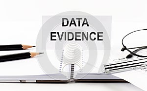 Text DATA EVIDENCE on paper card,pen, pencils, glasses,financial documentation on table - business concept