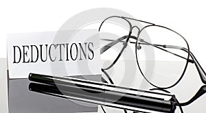 Text DEDUCTIONS on white sticker paper on light background with pen and glasses. Business concept