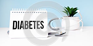 The text DIABETES is written on notepad near a stethoscope on a blue background. Medical concept