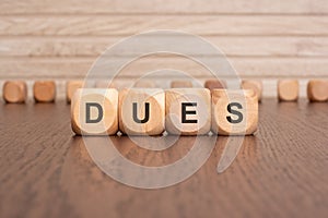 the text DUES is written on wooden cubes on a brown background