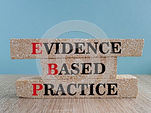 Text EBP Evidence-based practice concept on brick blocks. Beautiful blue background, wooden table.