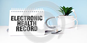 The text ELECTRONIC HEALTH RECORD is written on notepad near a stethoscope on a blue background. Medical concept