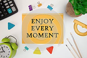 Text Enjoy Every Moment. Inspirational quotes on notebook and office supplies