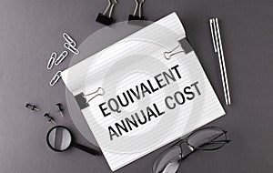 Text EQUIVALENT ANNUAL COST on Notebook and office tools on gray desktop