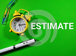 Text ESTIMATE with clock,pen and paperclips on a green background.Business concept.
