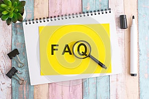 text FAQ under a magnifying glass on a yellow background, top view, the text is written in black marker