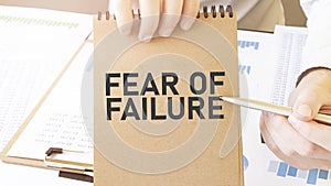 Text FEAR OF FAILURE on brown paper notepad in businessman hands on the table with diagram. Business concept