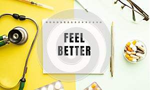 Text FEEL BETTER on notebook with stethoscope and pen on yellow background.