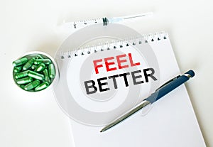 Text Feel Better written in a notebook with a blue pen and a bunch of pills