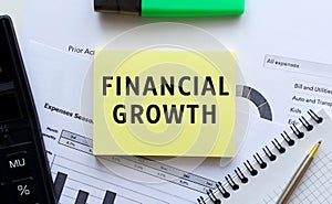 Text FINANCIAL GROWTH on the page of a notepad lying on financial charts on the office desk
