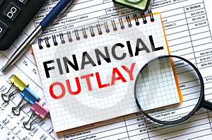 Text Financial Outlay on notepad with calculator, clips, pen on financial report