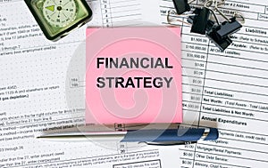 Text Financial Strategy on note paper with pen, compass and paper clips