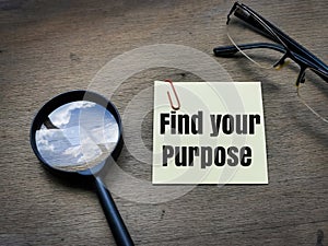 text Find your purpose on sticky note with magnifying glass and eye glasses on wooden background.