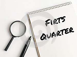 Text FIRST QUARTER on notebook with magnifying glass and marker pen.