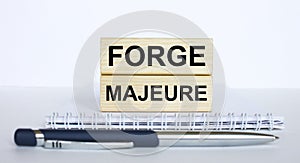 The text Forge Majeure on a bar of jenga wood, lying on a Notepad with a metal blue pen