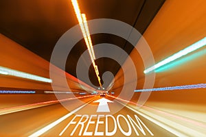 Text freedom and written on the straight road with an arrow in a tunnel with a blurred light.