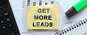 Text GET MORE LEADS on the page of a notepad lying on financial charts on the office desk