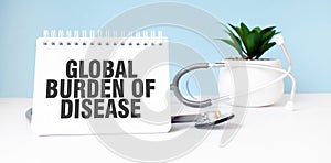The text GLOBAL BURDEN OF DISEASE is written on notepad near a stethoscope on a blue background. Medical concept
