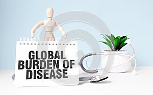The text GLOBAL BURDEN OF DISEASE is written on notepad and wood man toy near a stethoscope on a blue background. Medical concept