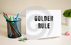 The text GOLDEN RULES is written on a white folded sheet of paper on the table. Nearby are pens and pencils.