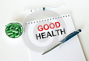 Text Good Health written in a notebook with a blue pen and a bunch of pills