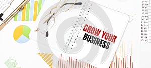 Text GROW YOUR BUSINESS on white notepad, glasses, graphs and diagrams