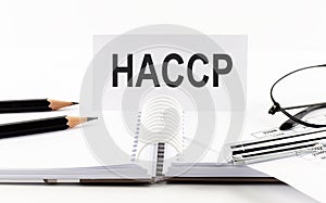 Text HACCP on paper card,pen, pencils, glasses,financial documentation on table - business concept